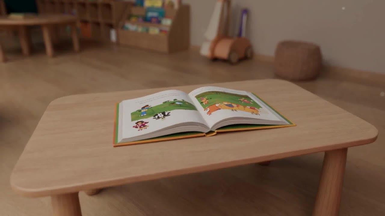 Concept render: an open picture book on a child-height wooden table in a classroom